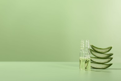 Skincare ampoules with extract of aloe vera and cut leaves on pale green background. Space for text