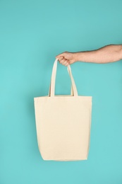 Man holding cotton shopping eco bag on color background. Mockup for design