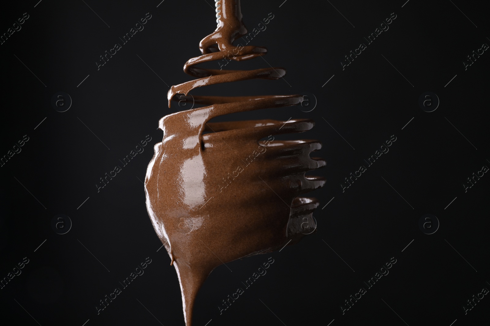 Photo of Chocolate cream flowing from whisk on black background, closeup