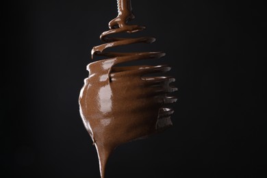 Photo of Chocolate cream flowing from whisk on black background, closeup