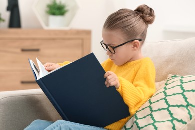 Photo of Cute little girl in glasses reading book indoors