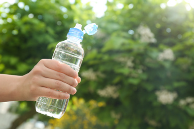 Photo of Young woman holding bottle of pure water outdoors, closeup. Space for text