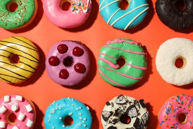 Sweet tasty glazed donuts on coral background, flat lay