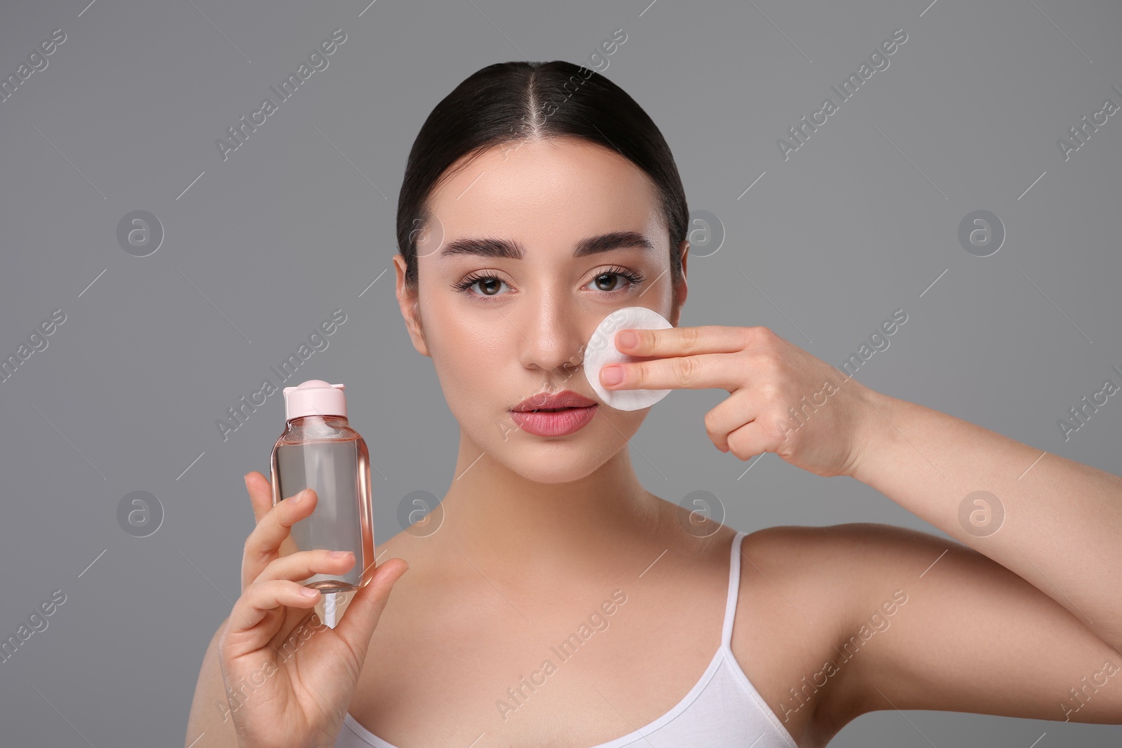 Photo of Beautiful woman removing makeup with cotton pad on gray background