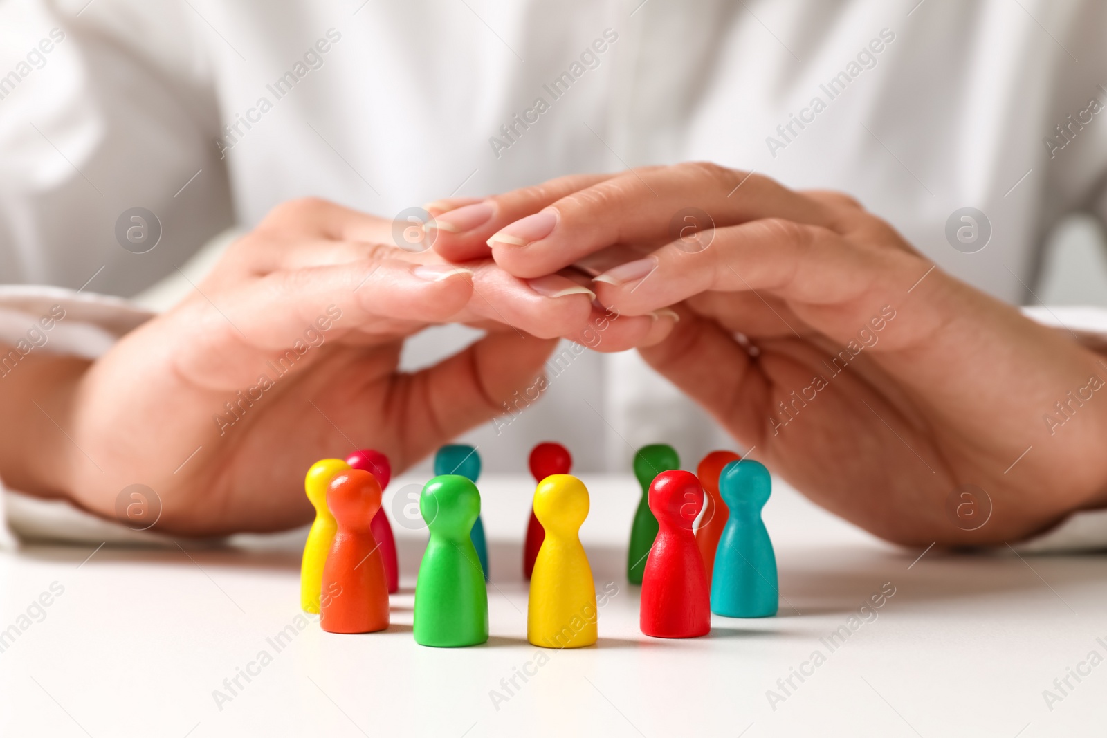 Photo of Woman sheltering colorful pawns at white table, closeup. Social inclusion concept