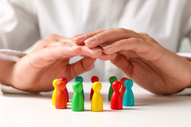 Photo of Woman sheltering colorful pawns at white table, closeup. Social inclusion concept