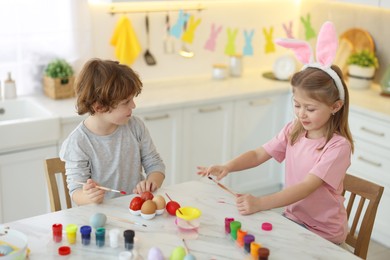 Easter celebration. Cute children with bunny ears painting eggs at white marble table in kitchen