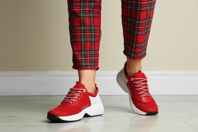 Photo of Woman wearing stylish sneakers near beige wall indoors, closeup