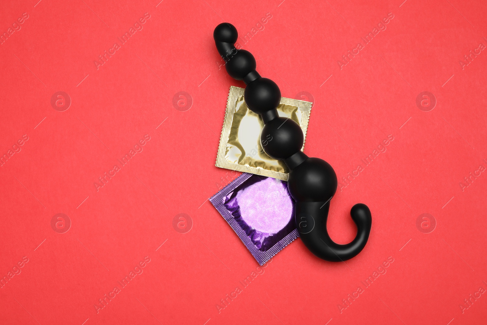 Photo of Anal ball beads and condoms on red background, top view. Sex game