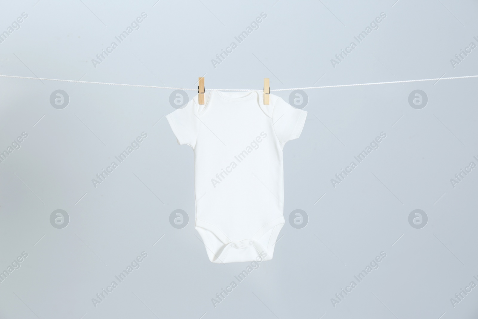 Photo of Cute baby onesie hanging on clothes line against light grey background. Laundry day