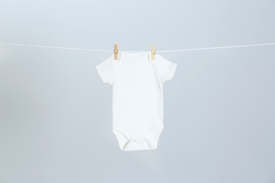 Photo of Cute baby onesie hanging on clothes line against light grey background. Laundry day