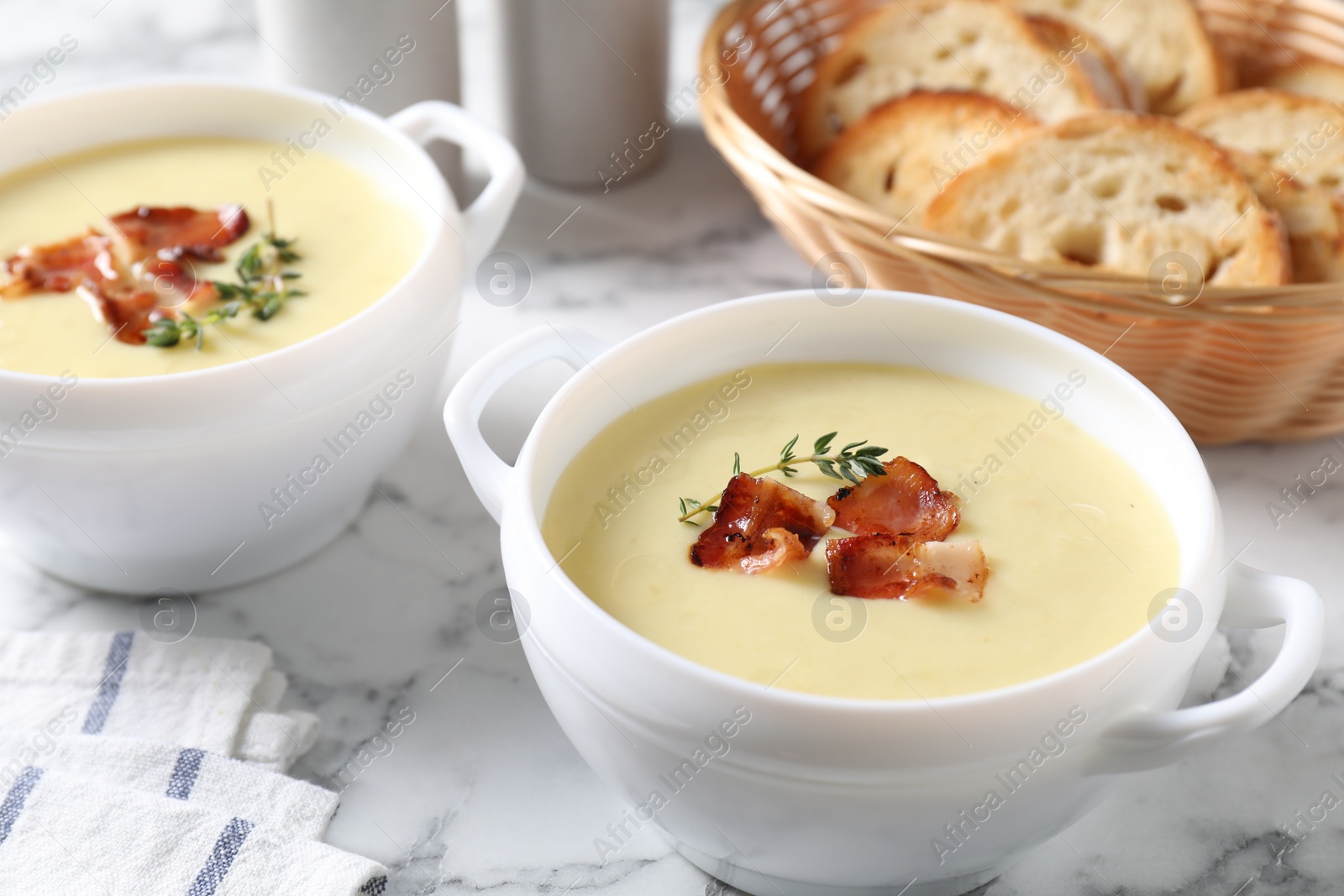 Photo of Tasty potato soup with bacon and rosemary in bowls on white marble table, closeup