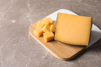 Board with delicious cut cheese on marble table. Space for text