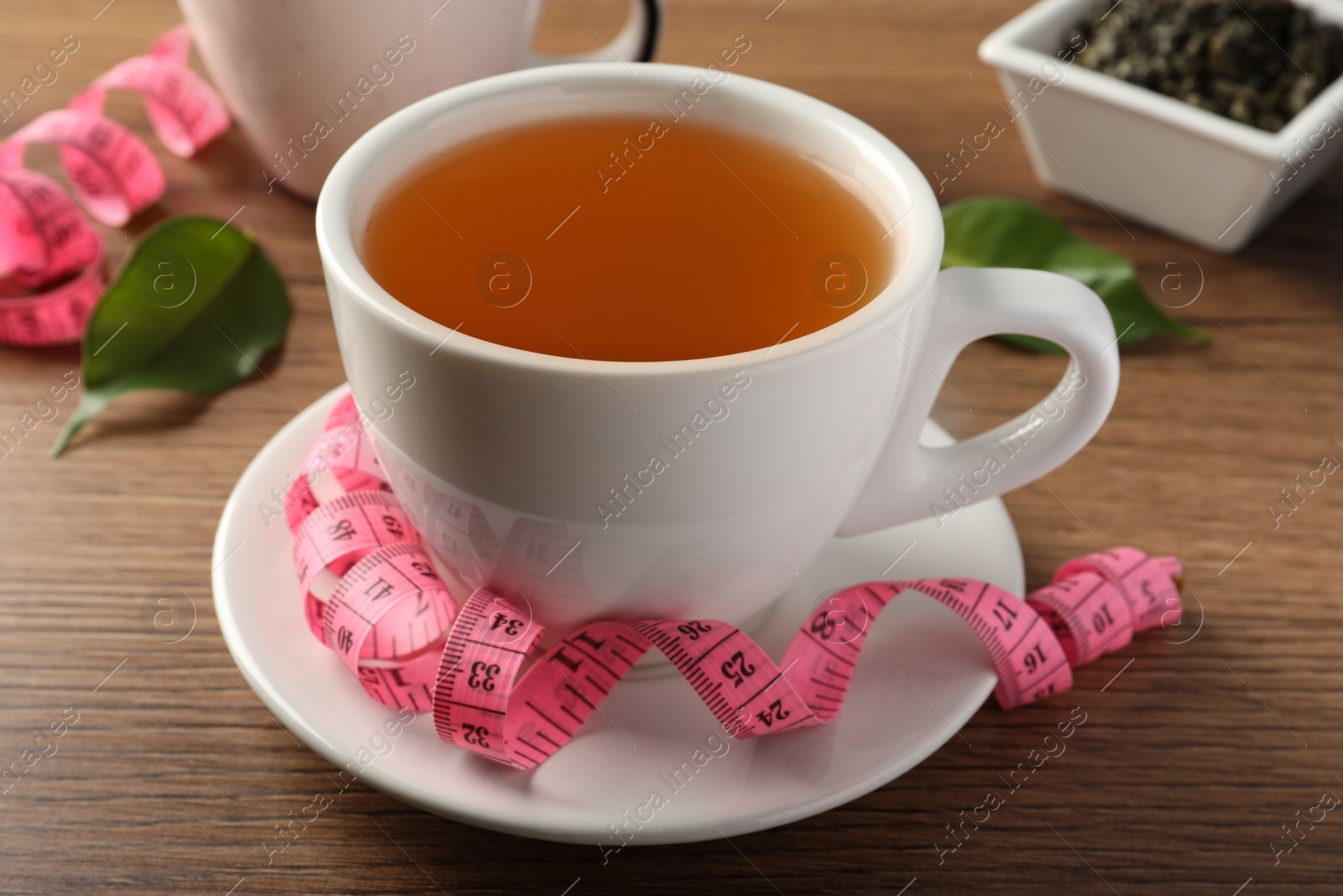 Photo of Cup of herbal diet tea and measuring tape on wooden table. Weight loss concept