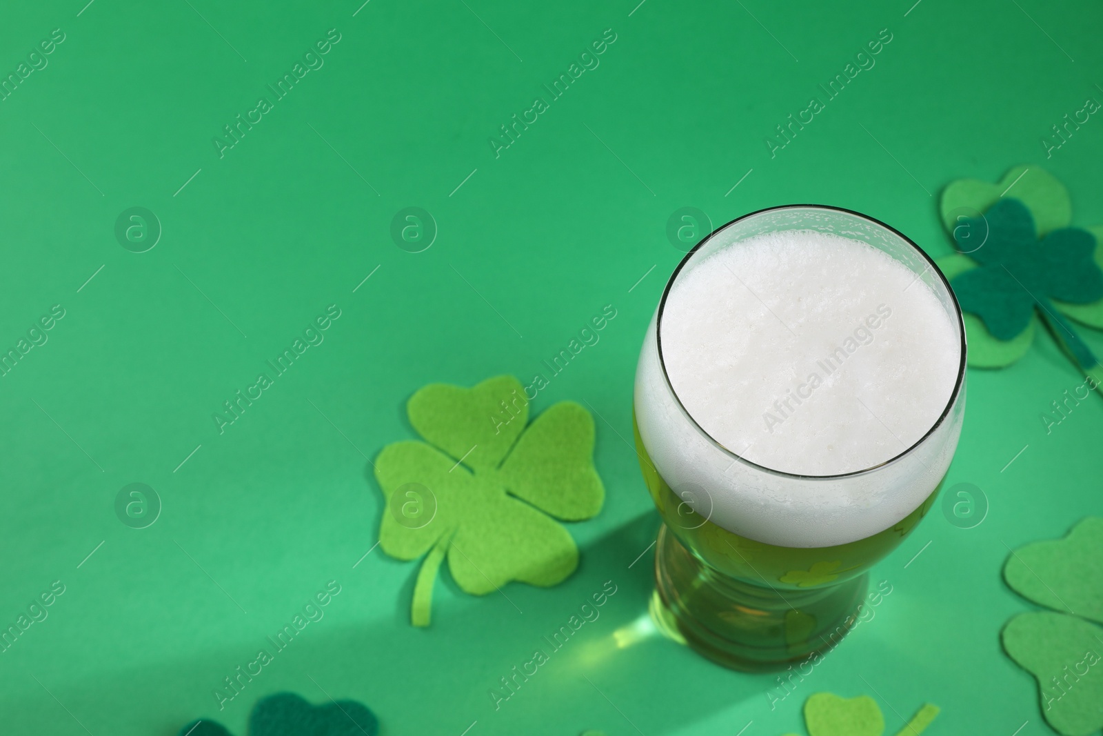 Photo of St. Patrick's day party. Green beer in glass and decorative clover leaves on green background, above view. Space for text