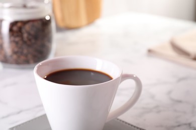 Photo of Delicious coffee in cup on white marble table, closeup. Space for text