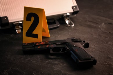 Photo of Gun with blood and evidence marker on black slate table, closeup. Crime scene