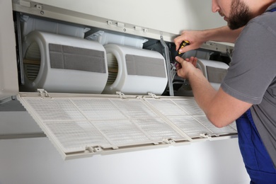 Photo of Young male technician repairing air conditioner indoors