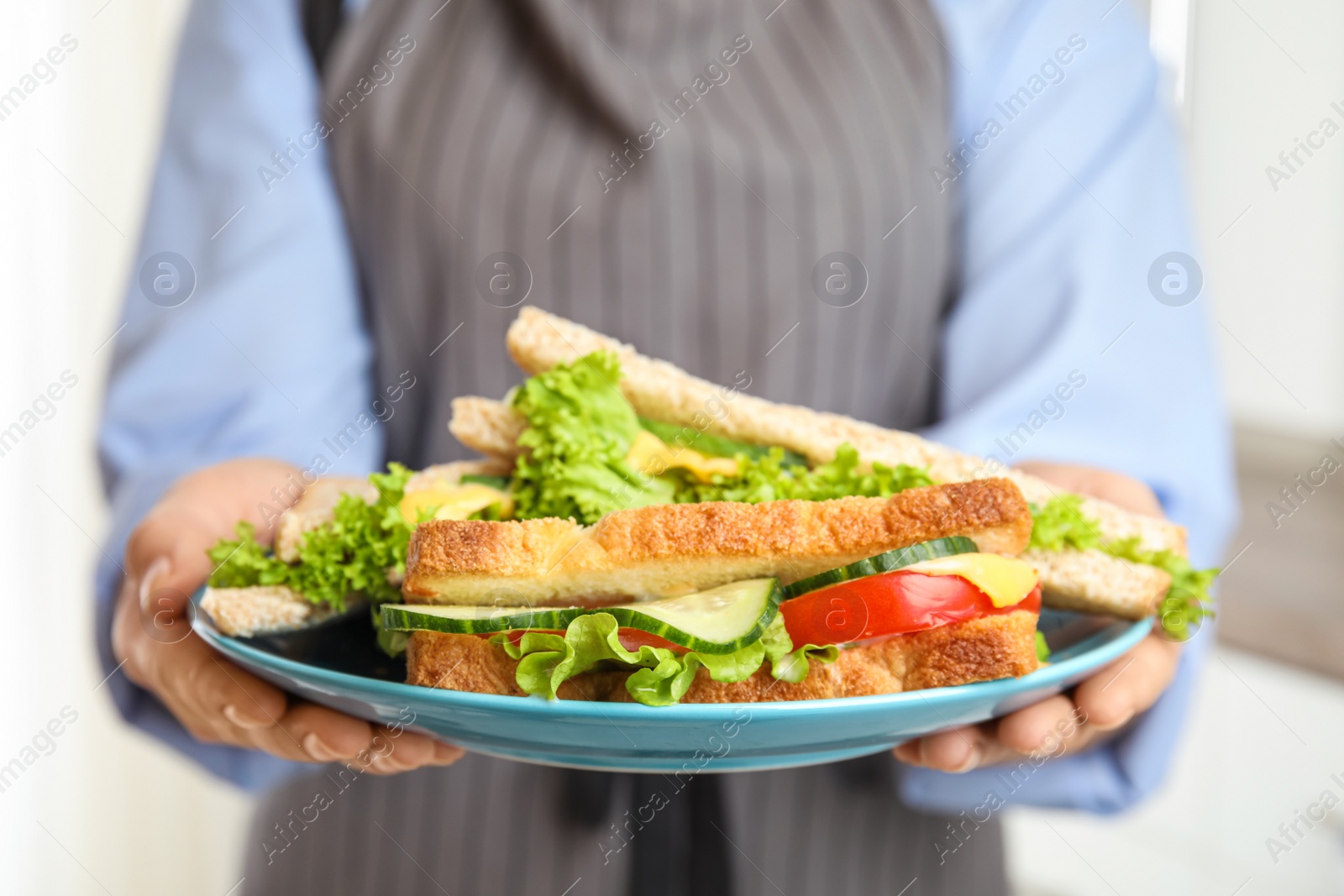 Photo of Woman holding plate with tasty sandwiches indoors, closeup