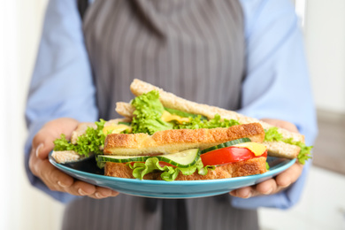 Photo of Woman holding plate with tasty sandwiches indoors, closeup