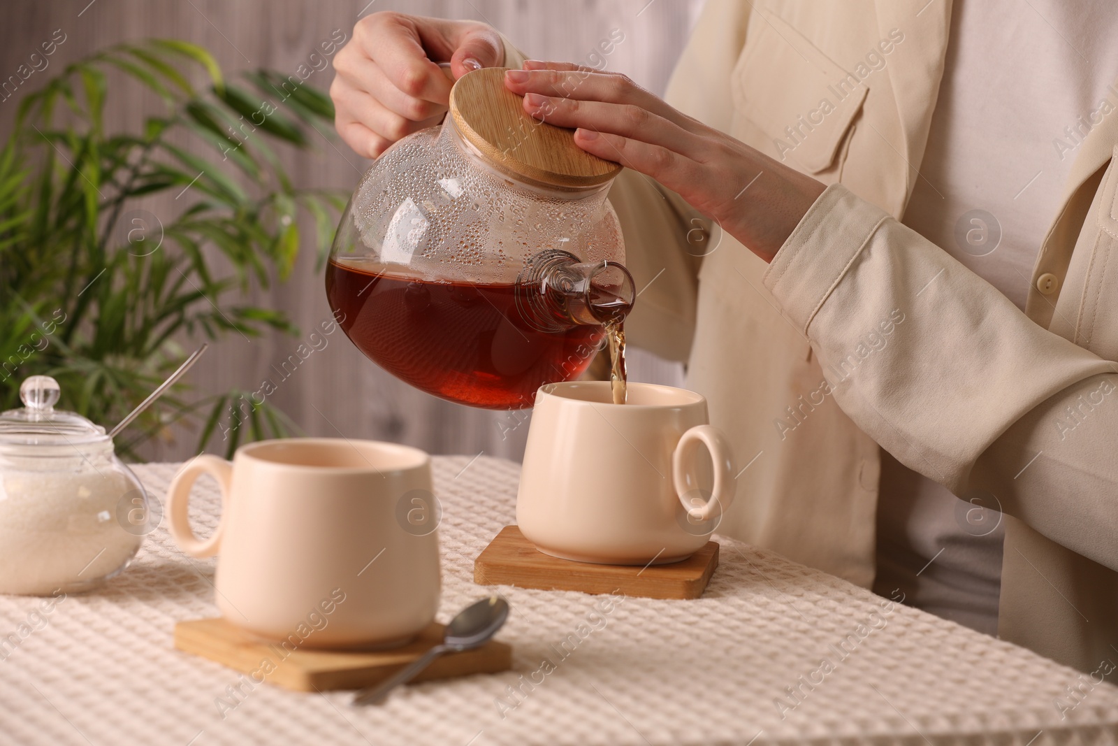 Photo of Woman pouring aromatic tea into cup at table, closeup