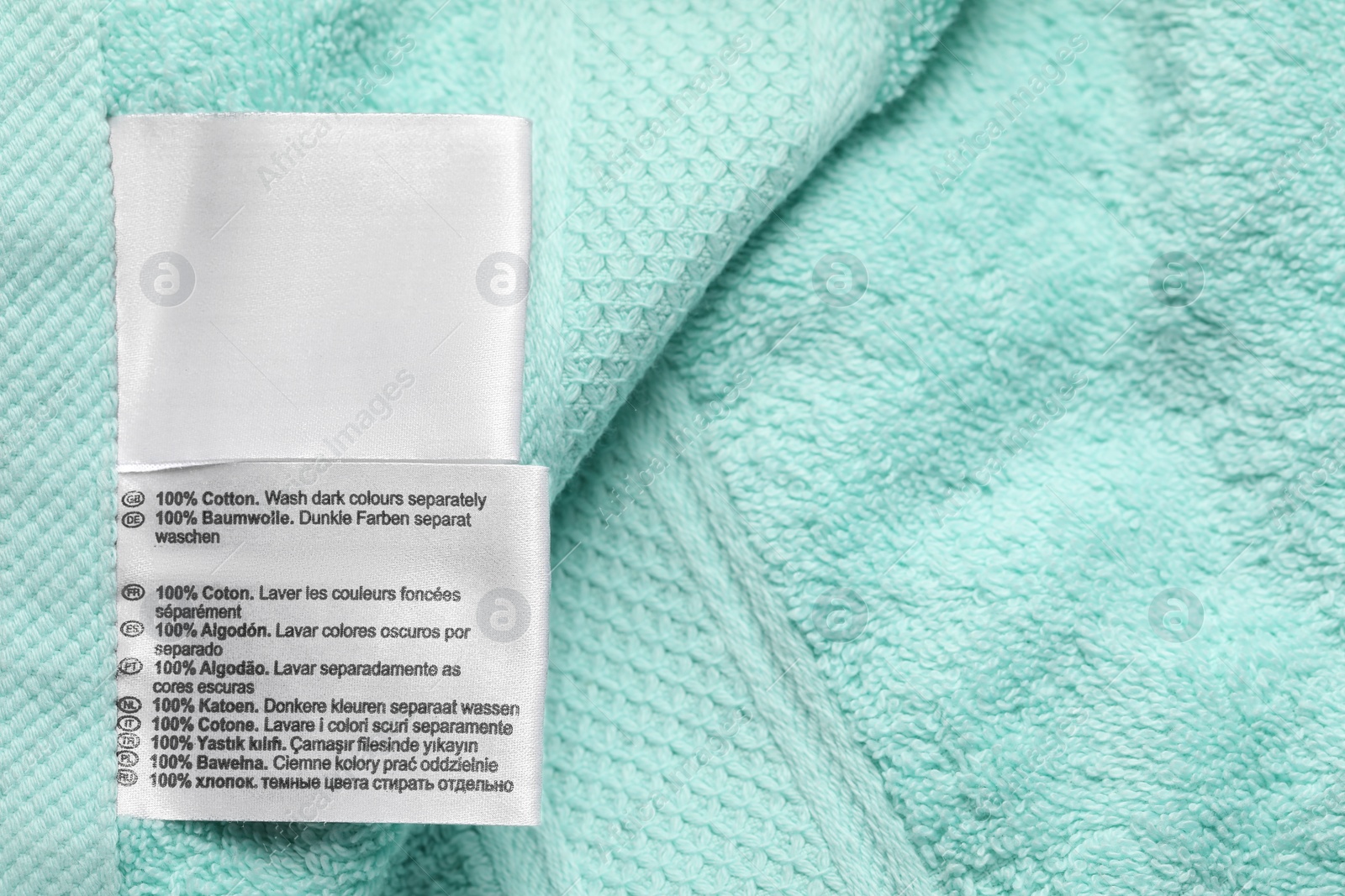 Photo of Clothing label on turquoise fluffy towel, top view. Space for text