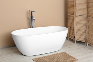 Photo of Beautiful white tub near beige wall in bathroom. Interior design