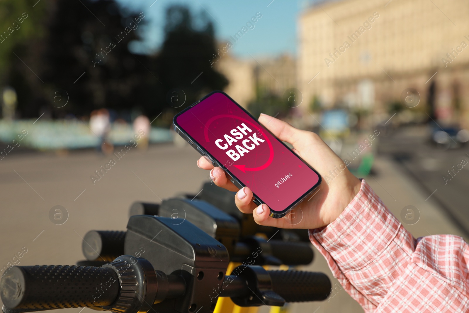 Image of Woman holding smartphone with word Cashback near electric kick scooter outdoors, closeup