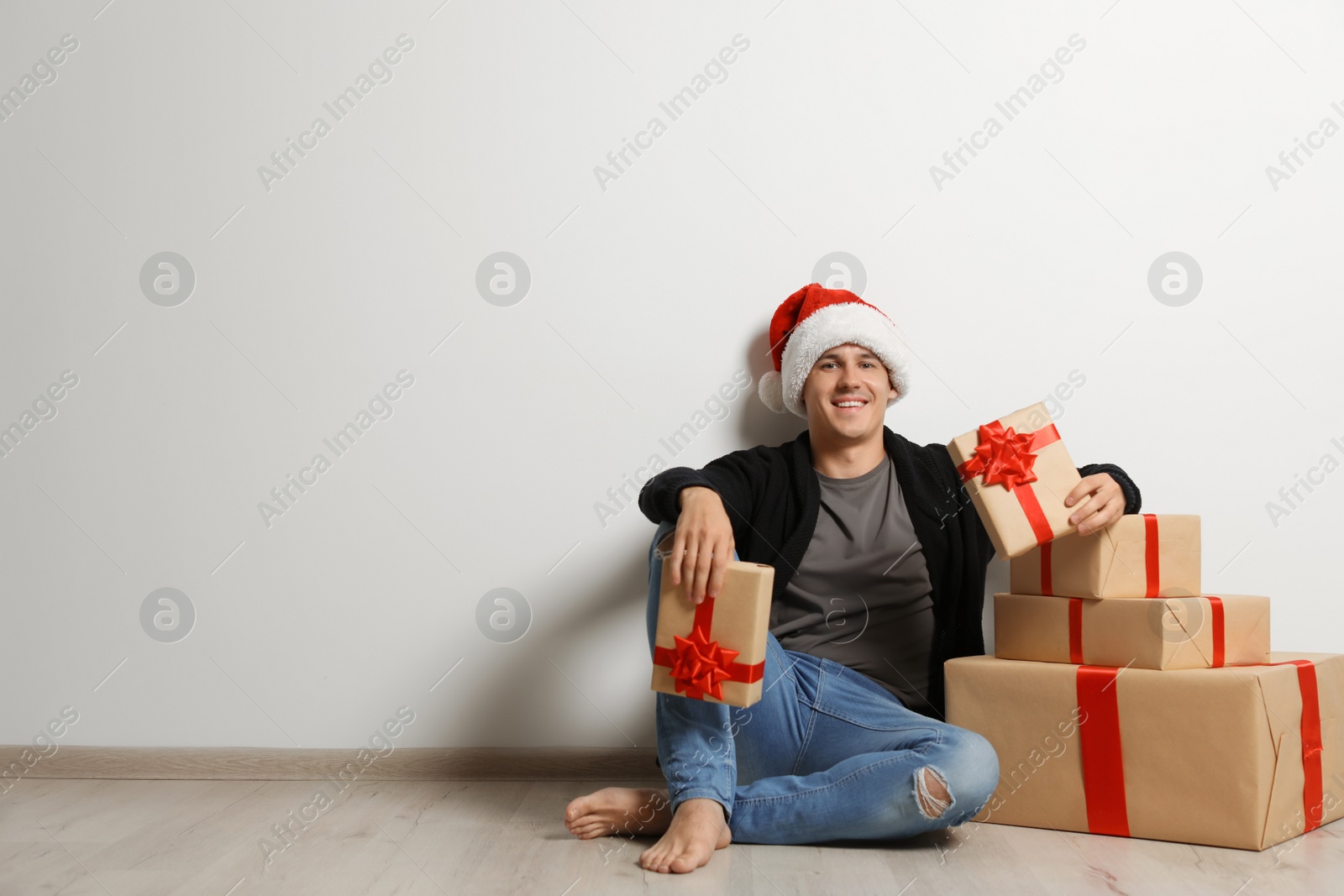 Photo of Young man with Christmas gifts near white wall