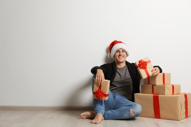 Photo of Young man with Christmas gifts near white wall