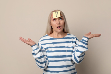 Photo of Emotional mature woman with question mark on beige background