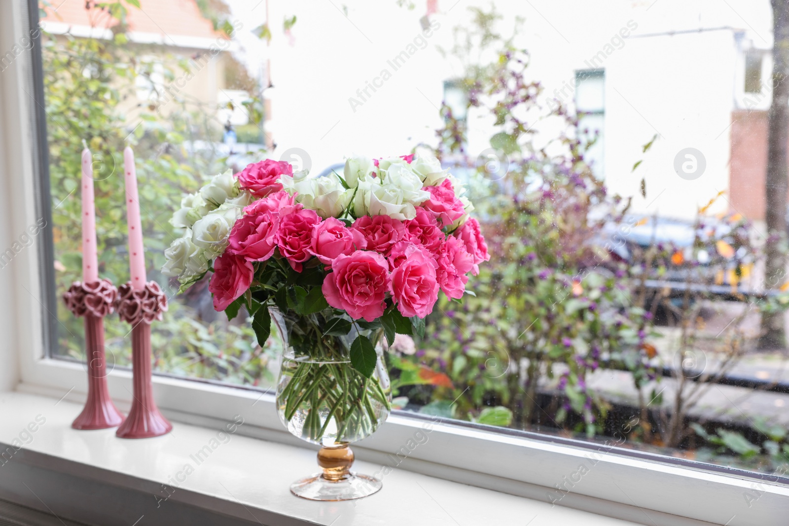 Photo of Vase with beautiful bouquet of roses and candles on windowsill indoors, space for text