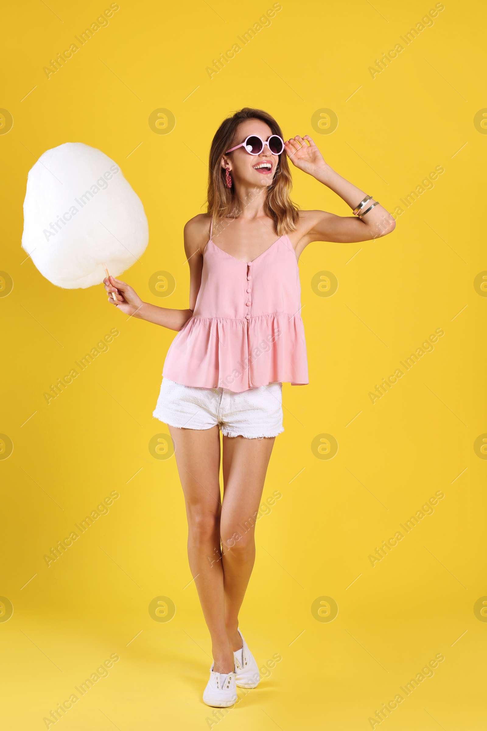 Photo of Happy young woman with cotton candy on yellow background