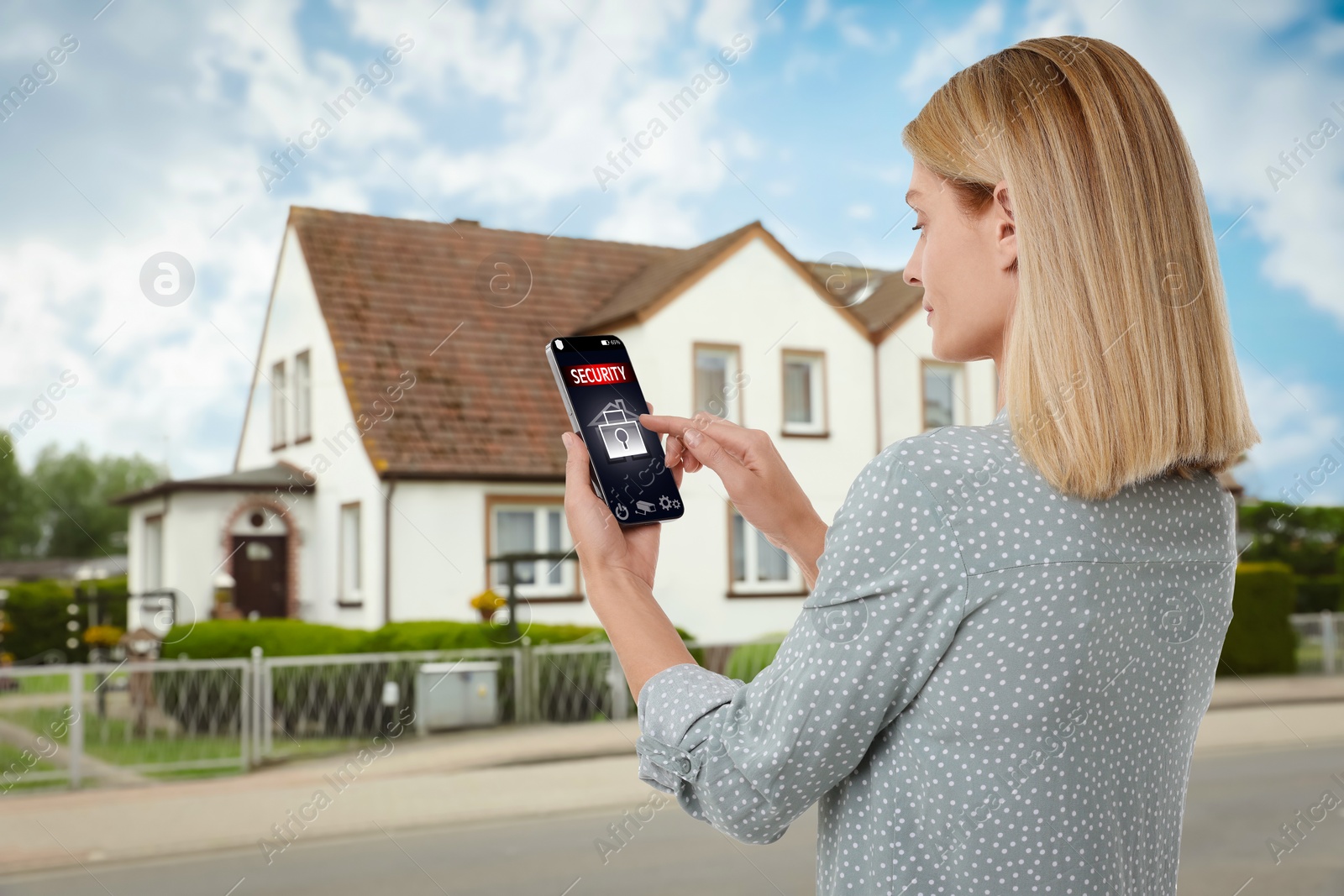 Image of Woman using home security system application on smartphone outdoors
