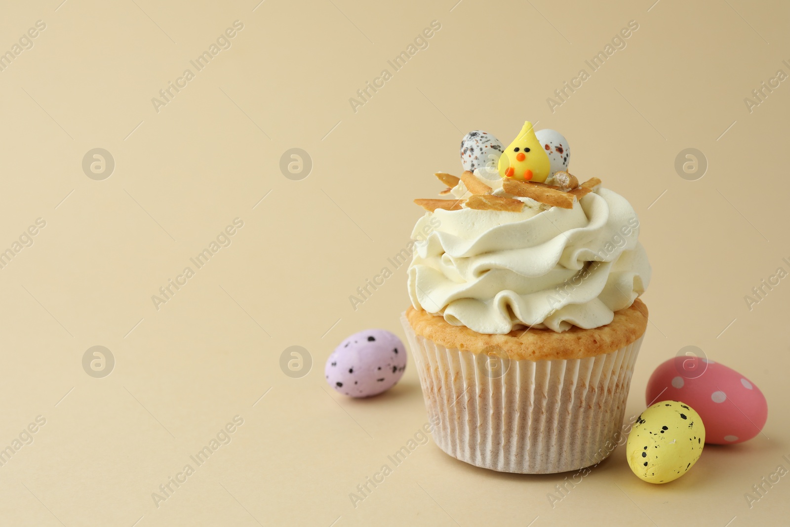 Photo of Tasty Easter cupcake with vanilla cream and candies on beige background, space for text