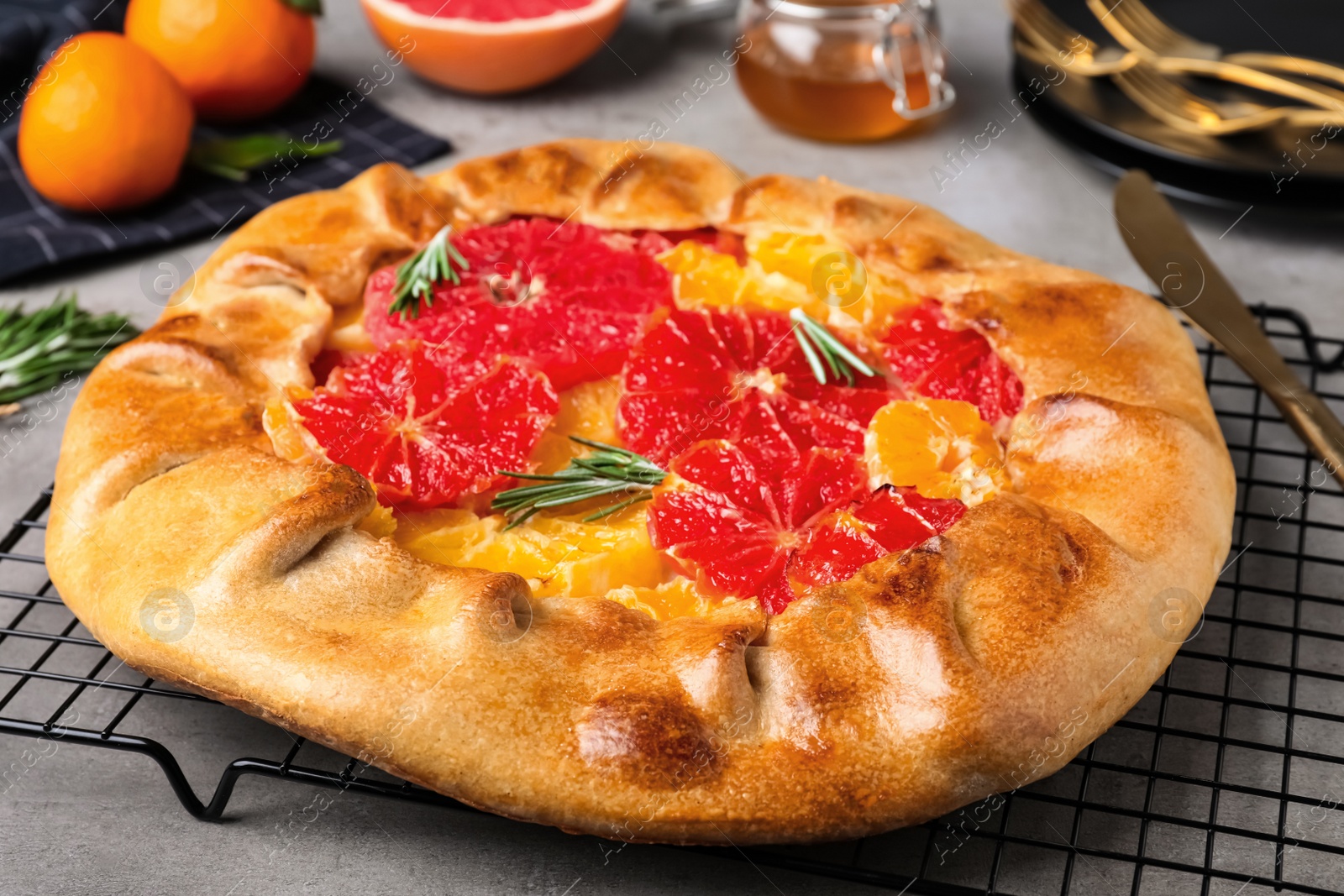 Photo of Tasty galette with citrus fruits and rosemary on grey table