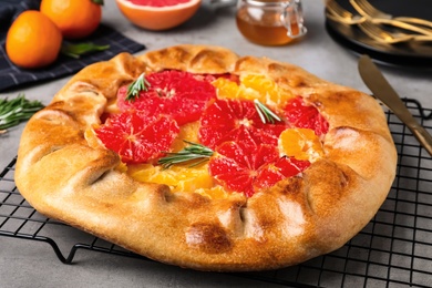 Photo of Tasty galette with citrus fruits and rosemary on grey table