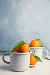 Photo of Fresh ripe tangerines with green leaves and mugs on table. Space for text