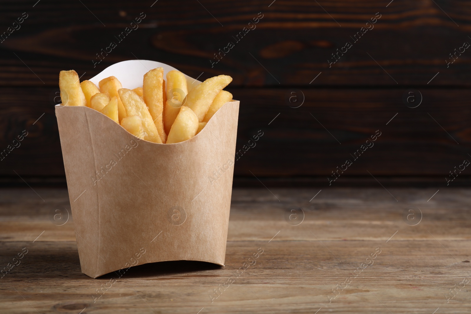 Photo of Delicious French fries in paper cup on wooden table, space for text