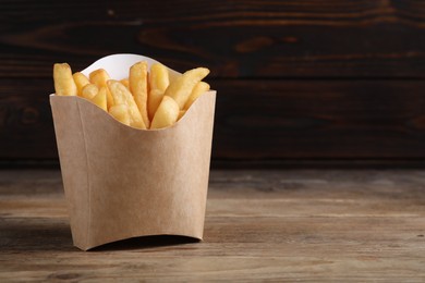 Photo of Delicious French fries in paper cup on wooden table, space for text