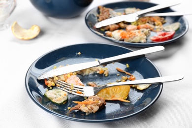 Photo of Plate with food leftovers on white tablecloth after party, closeup