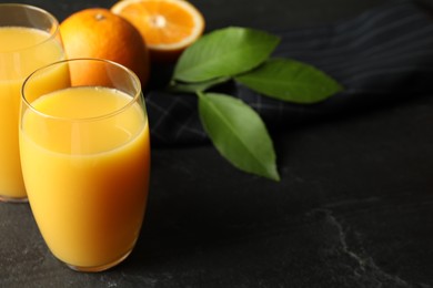 Photo of Glasses of orange juice and fresh fruits on black table. Space for text