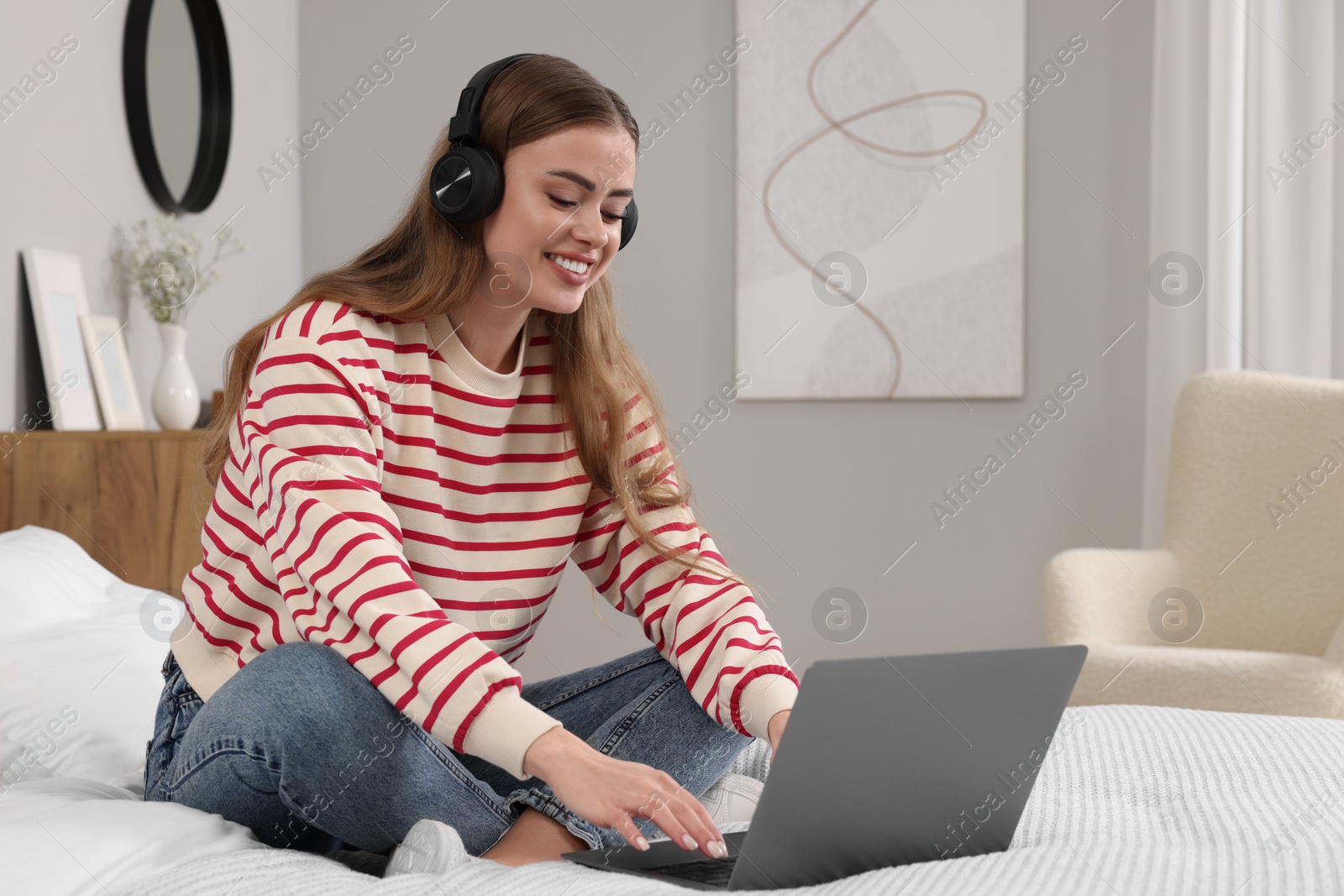 Photo of Happy woman with headphones and laptop on bed in bedroom