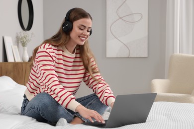Happy woman with headphones and laptop on bed in bedroom