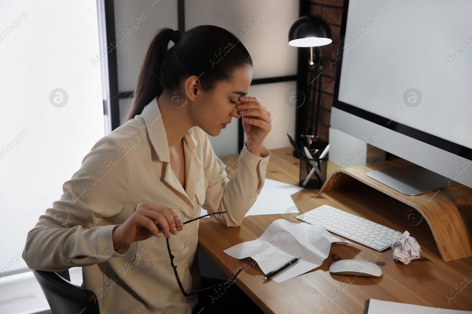 Photo of Stressed and tired young woman with headache at workplace