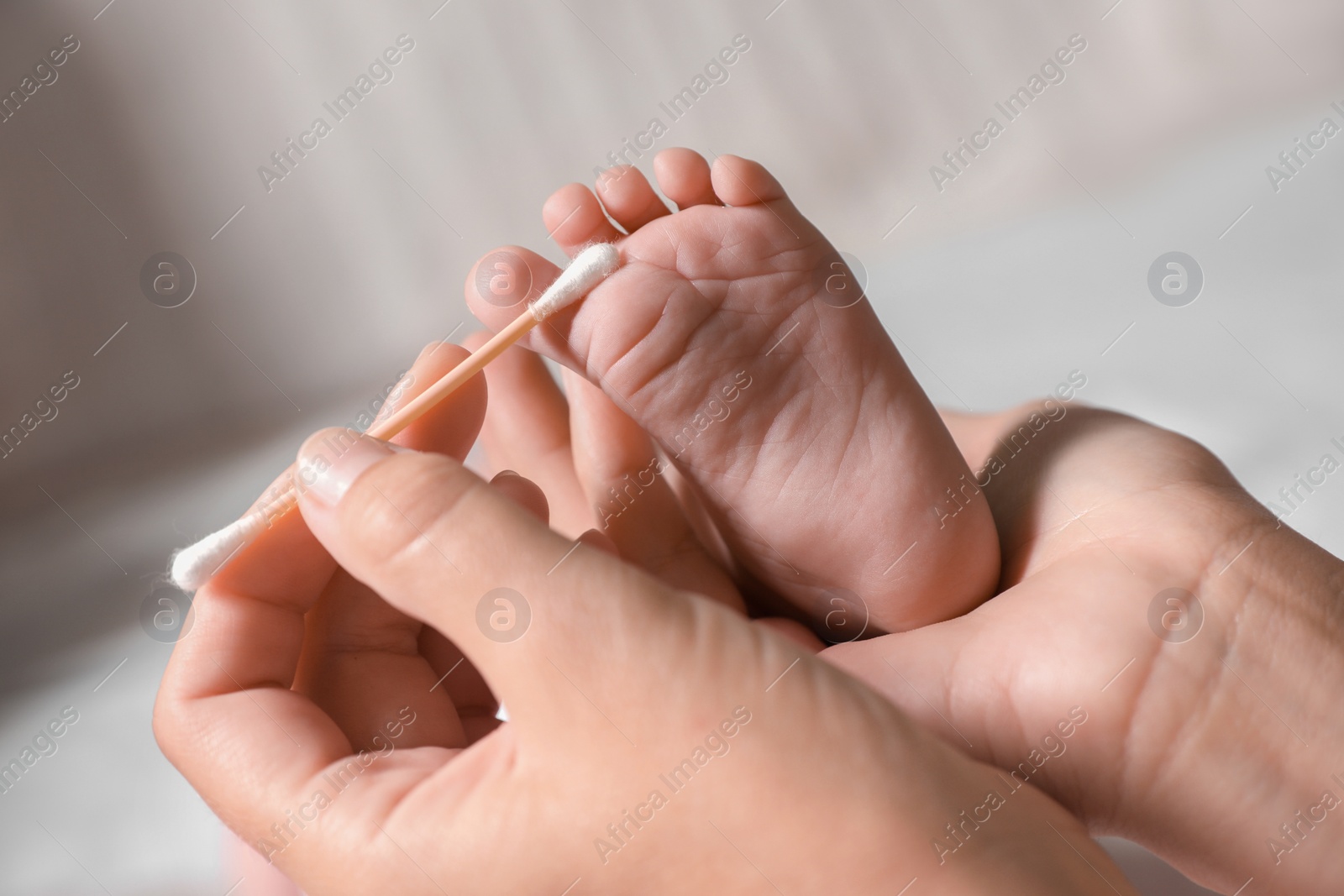 Photo of Mother cleaning baby`s foot with cotton bud on blurred background, closeup