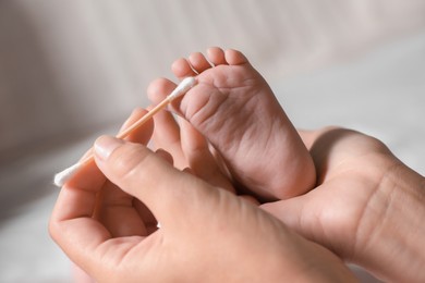 Mother cleaning baby`s foot with cotton bud on blurred background, closeup