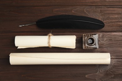 Photo of Feather pen, inkwell and paper rolls on wooden table, flat lay