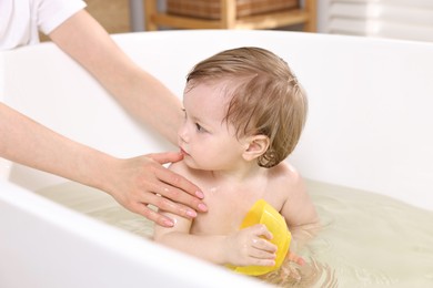 Photo of Mother bathing her cute little baby in tub at home