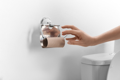 Photo of Woman reaching for empty toilet paper roll in bathroom, closeup